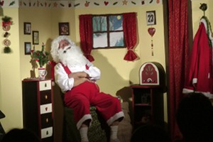 Der Weihnachtsmann schlummert auf einem Sessel in seinem Haus. Er ist klassisch rot-weiss gekleidet und hat einen langen, weissen Bart.