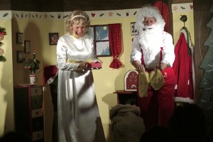 Christkind und Weihnachtsmann stehen auf der Bühne. Der Weihnachtsmann zeigt seine Nikolausstiefel – es sind eher Hausschuhe.
