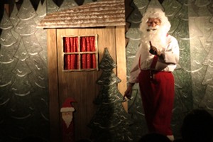 Der Weihnachtsmann steht vor seinem Nikolaushaus im Wald und spricht mit den Kindern.
