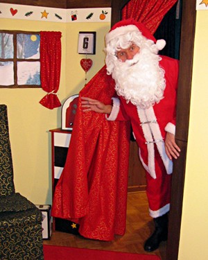 Der Weihnachtsmann schiebt einen roten
				Vorhang zur Seite und schaut durch die Tür in sein
				Wohnzimmer herein. Darin Sessel, Fenster mit Blick auf
				eine winterliche Landschaft und Kalenderblatt mit dem 6.
				Dezember.