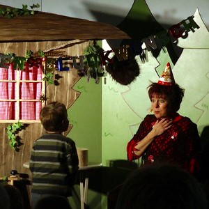 Hexe Schmusemund spricht mit einem Jungen aus dem Publikum. Hexe Schmusemund trägt einen spitzen Geburtstagshut auf dem Kopf.